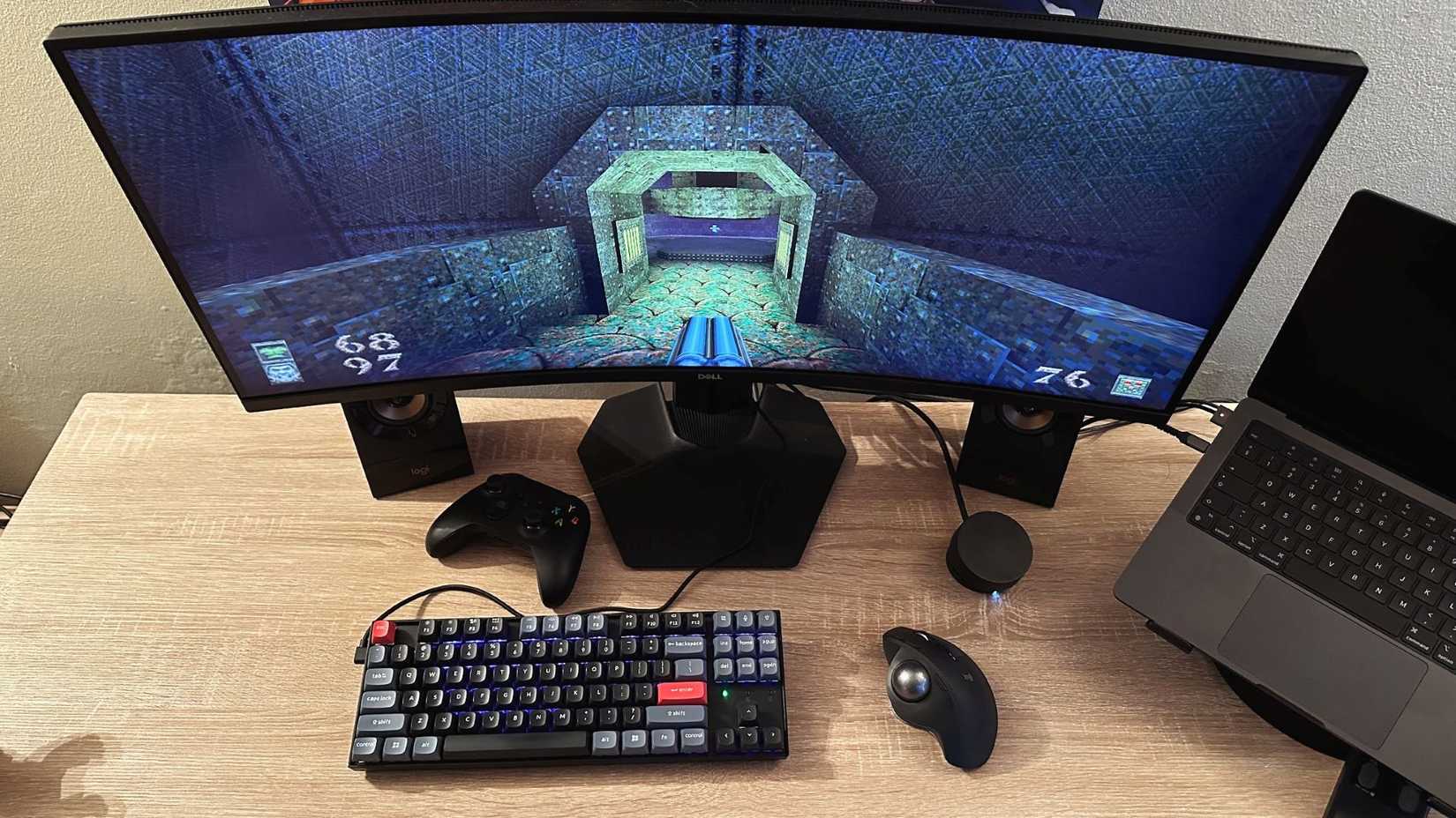 A table with a game console displaying Quake on the screen, and a mouse with a trackball.