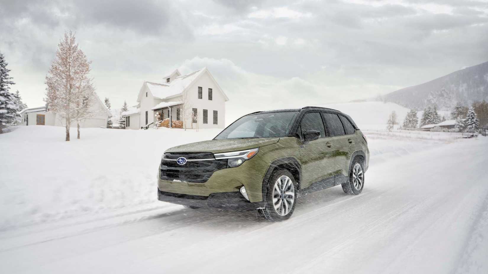 Dynamic front 3/4 shot of a green 2025 Subaru Forester Hybrid driving on a snow-covered road past a house.