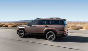 Dynamic side profile shot of a bronze 2025 Hyundai Santa Fe Hybrid driving on a country road through the desert.