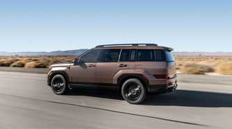 Dynamic side profile shot of a bronze 2025 Hyundai Santa Fe Hybrid driving on a country road through the desert.