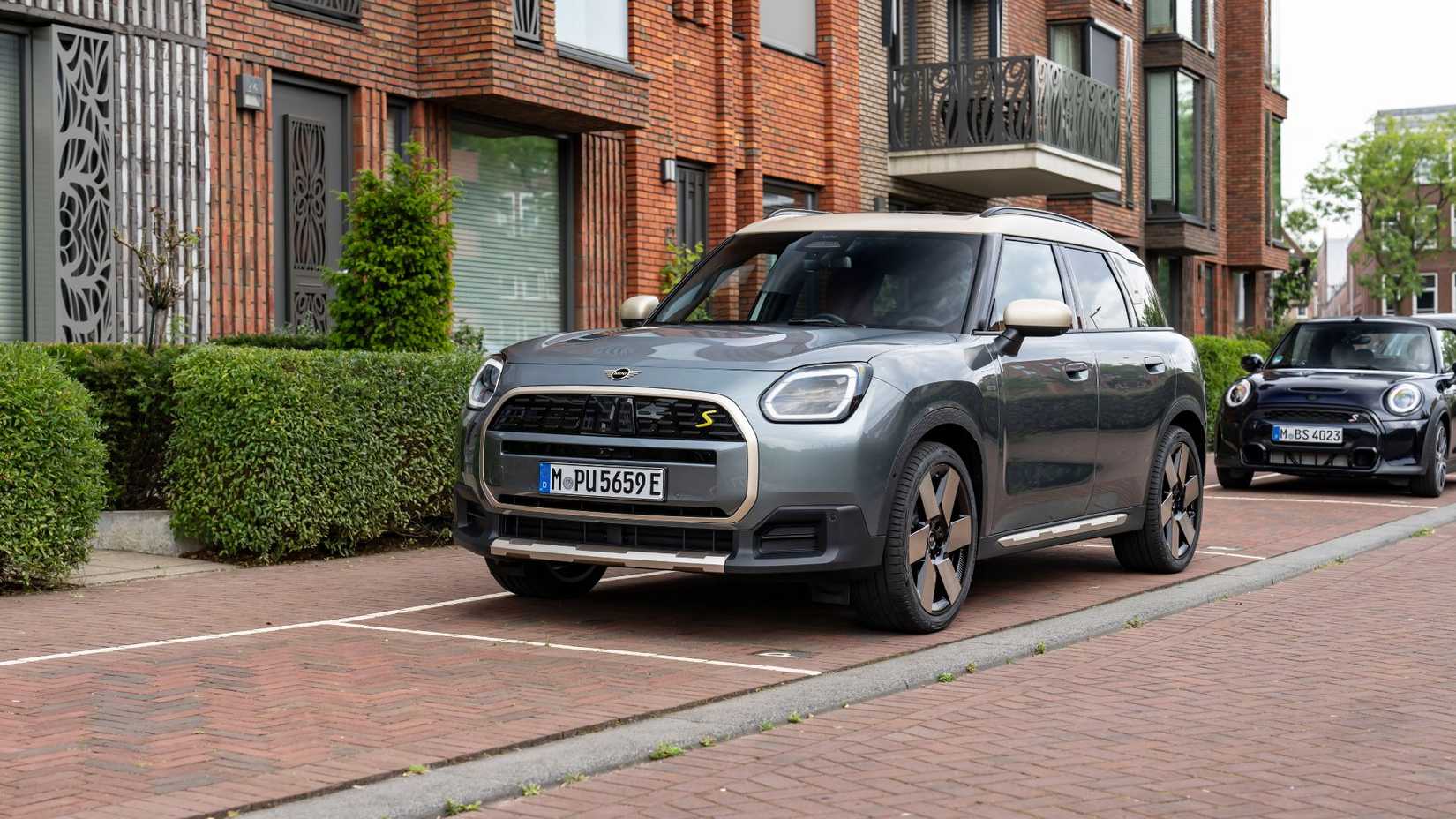 Static front 3/4 shot of a gray 2025 Mini Countryman SE All4 parked outside of a residential building.