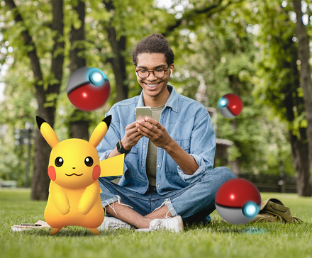 Young man sitting on the grass using his phone, surrounded by floating Poké Balls, with a Pikachu beside him.