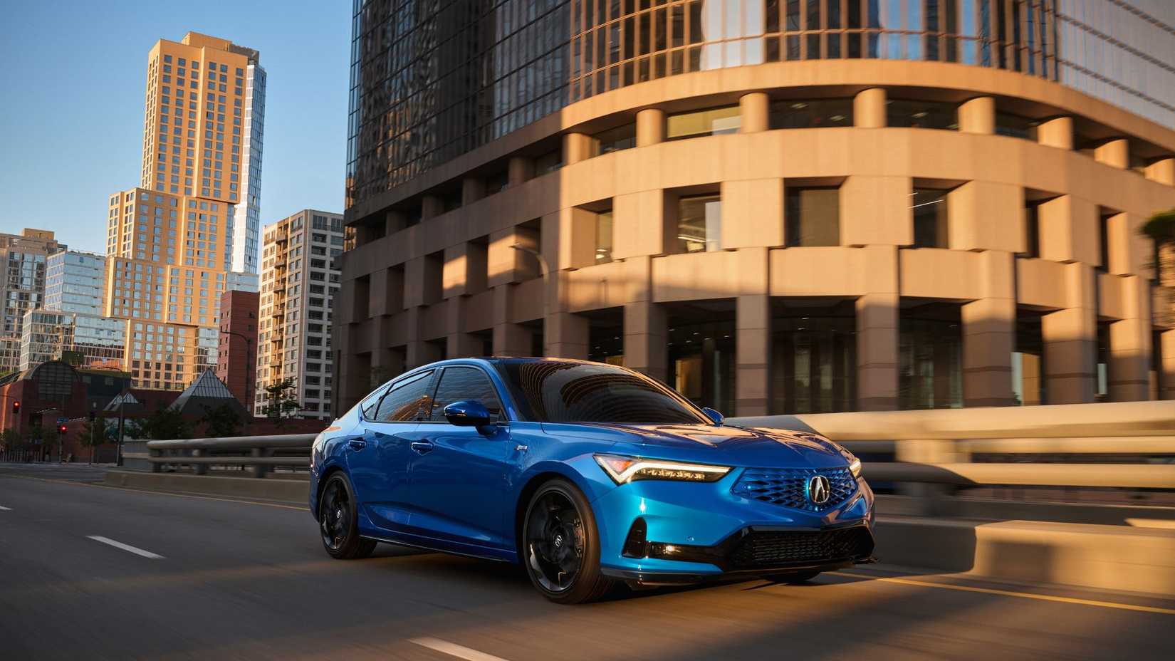 Toma dinámica de 3/4 del frente de un Acura Integra 2026 azul conduciendo en una ciudad.