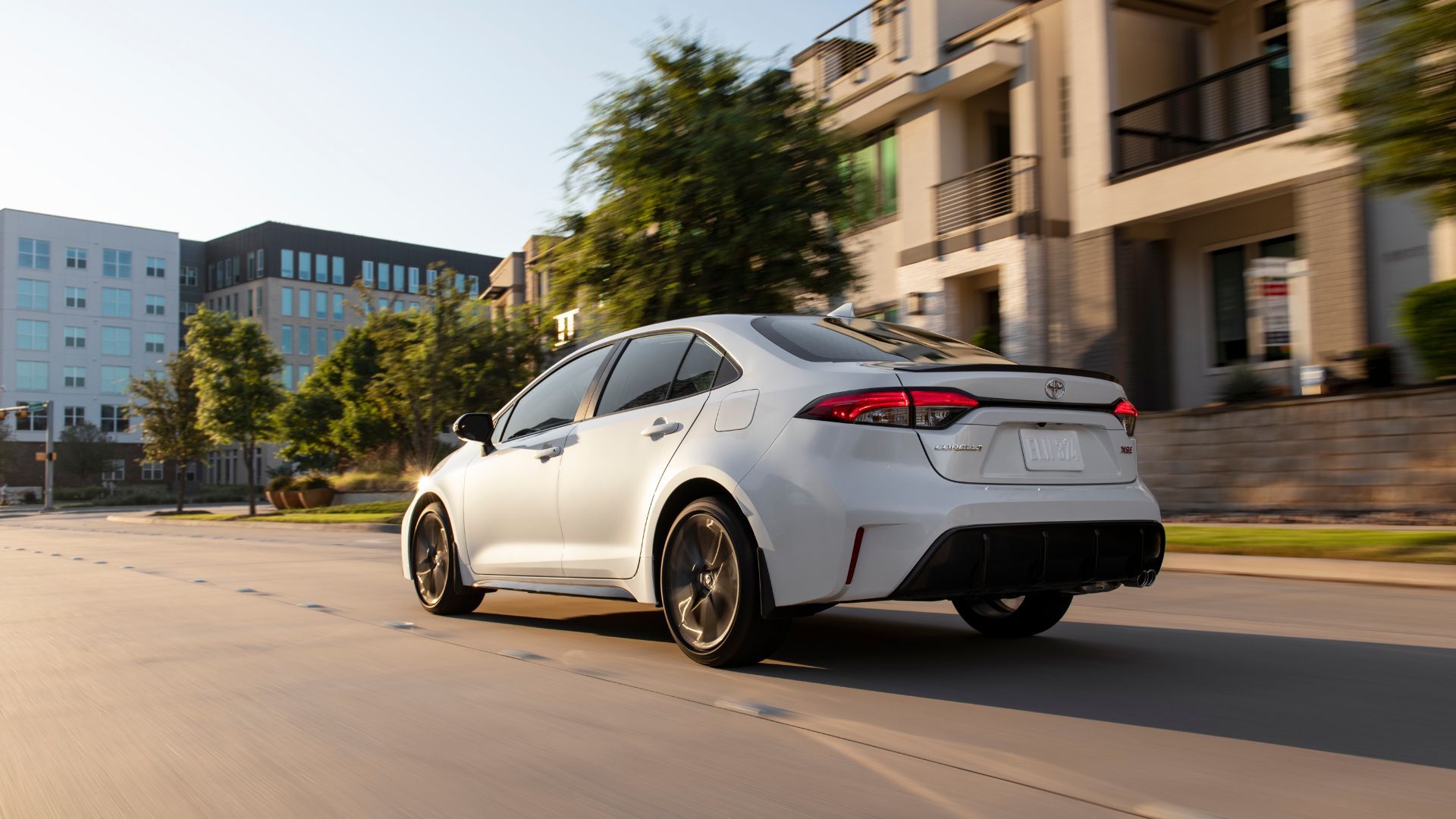Dynamic rear 3/4 shot of a white 2025 Toyota Corolla XSE driving through town.