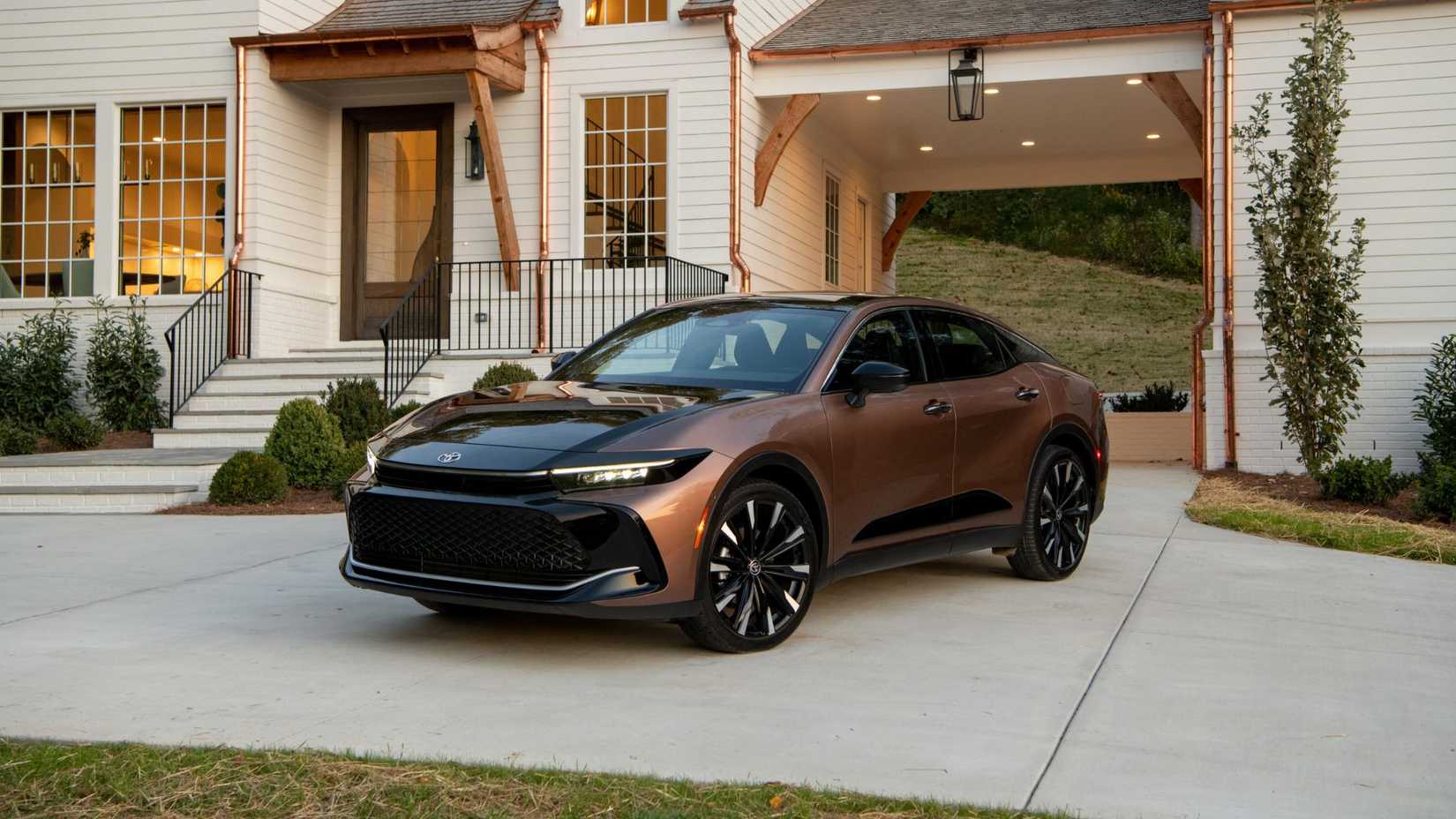 Static front 3/4 shot of a bronze 2026 Toyota Crown Platinum parked outside of a house.