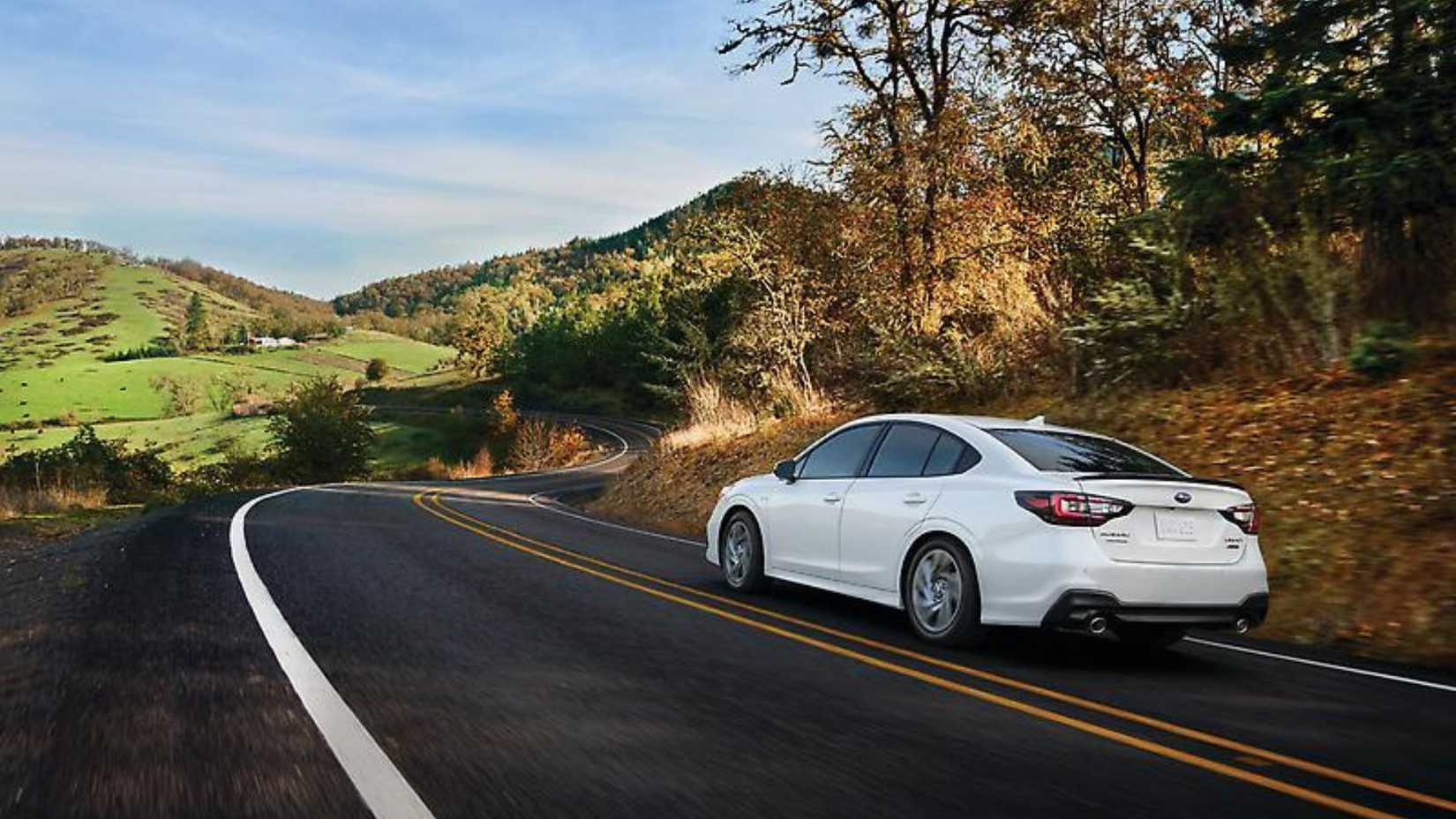 Dynamic rear 3/4 shot of a white 2024 Subaru Legacy driving on a country road.