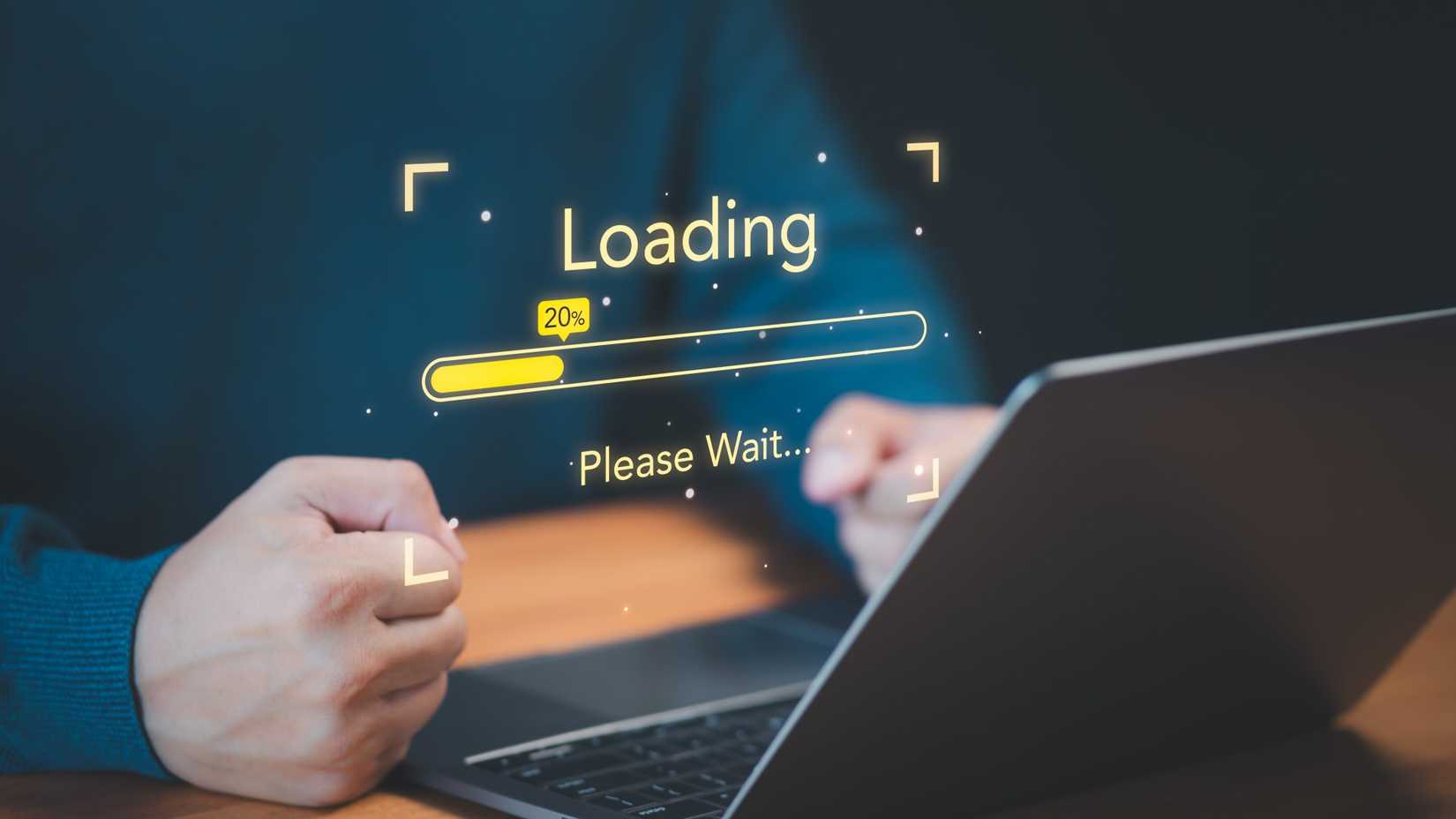 A person using a laptop with fists clinched in frustrating and a loading progress bar floating above the laptop.