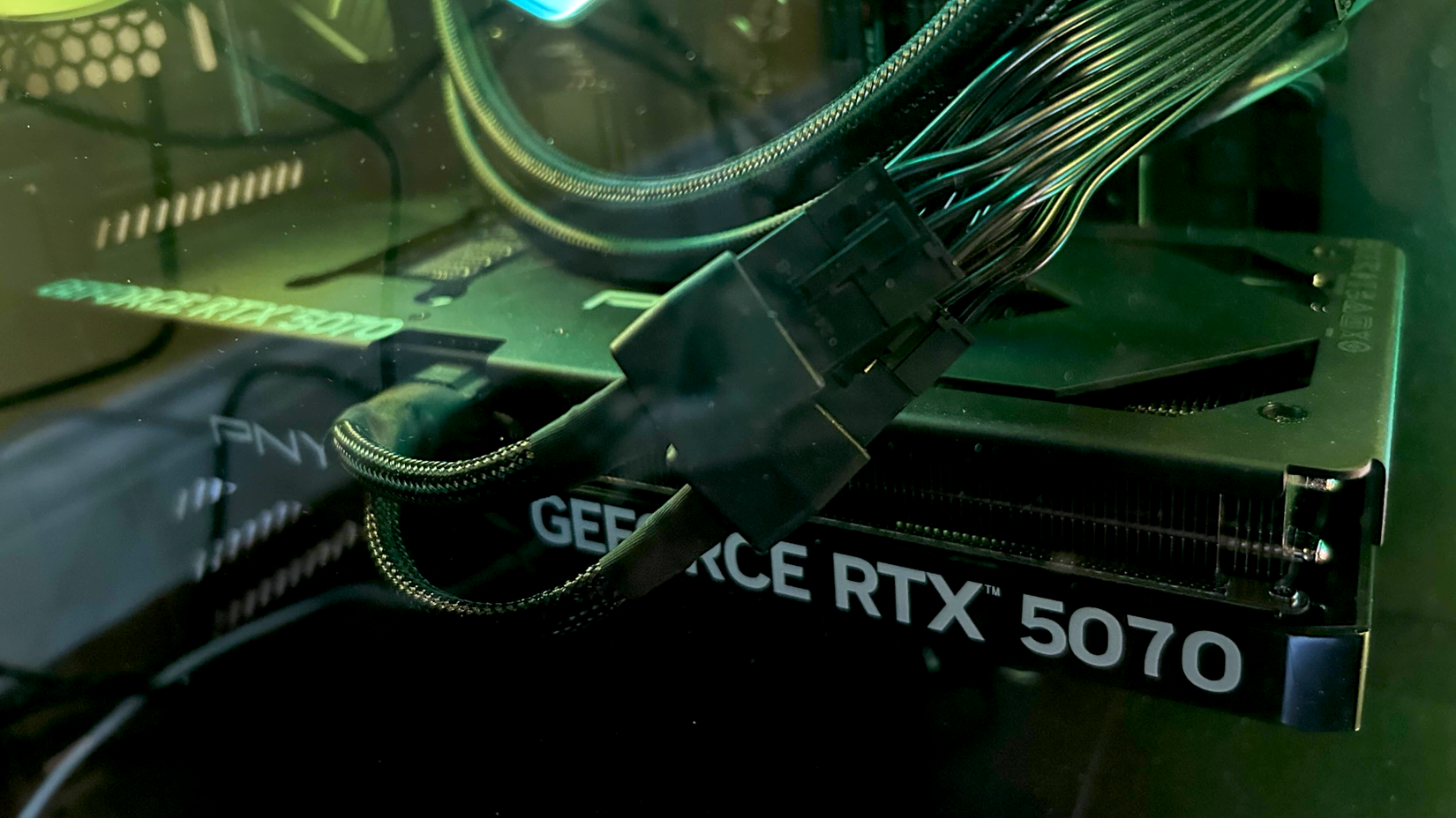 A GeForce RTX 5070 card inside of a PC tower illuminated by neon green light
