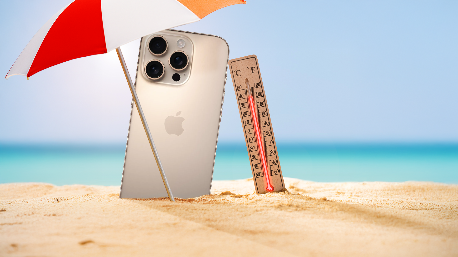 Um iPhone e um termômetro na areia sob um guarda-sol, com o oceano ao fundo.