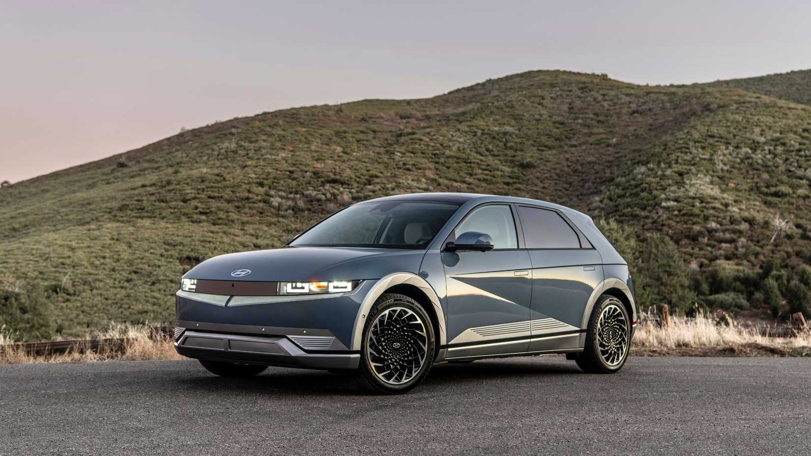 TOMA ESTÁTICA 3/4 de un Hyundai Ioniq 5 Green 2023 estacionado en la asfalto con una colina en el fondo.