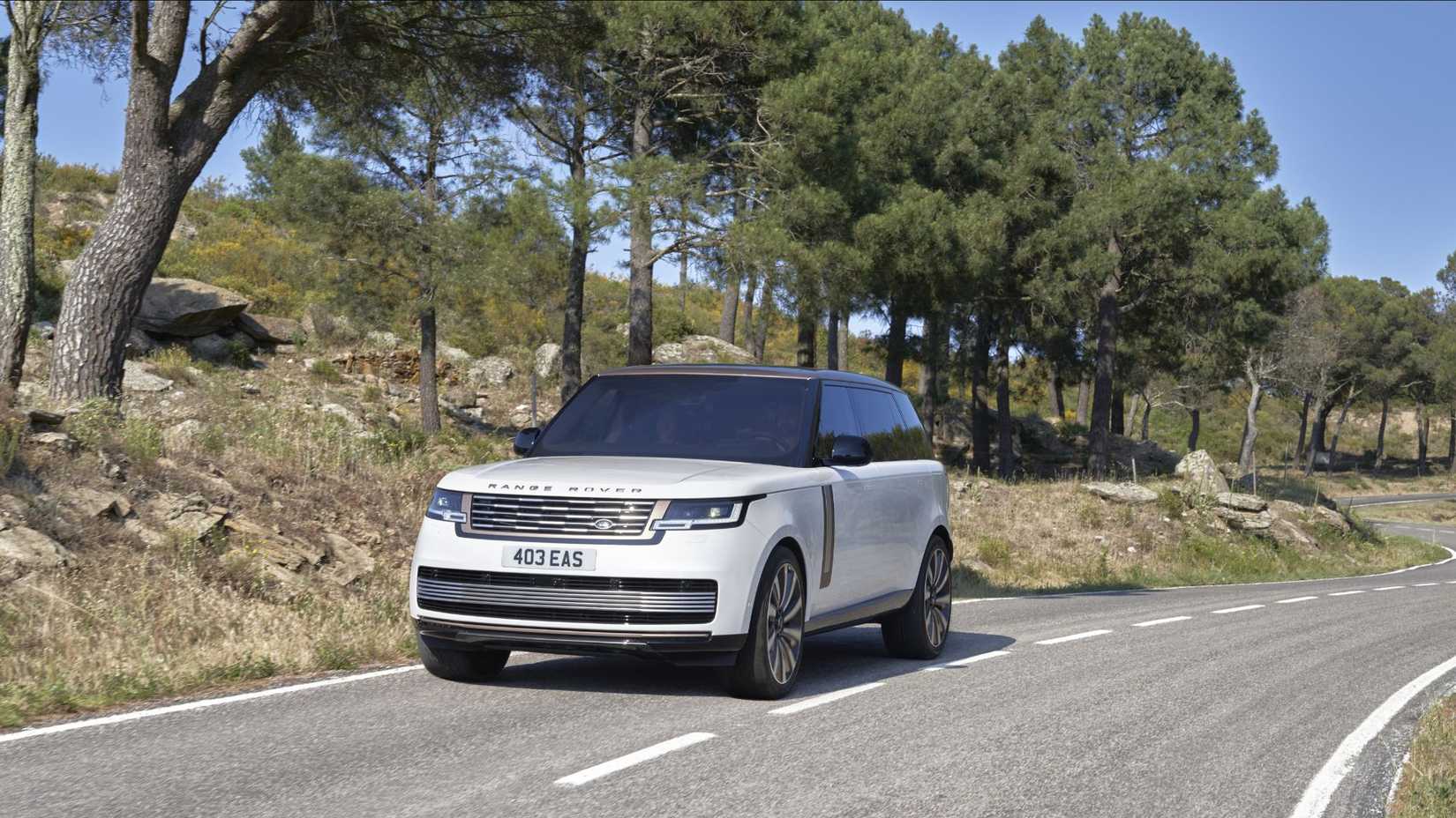 Frente dinâmica 3/4 Tiro de uma serenidade branca 2022 Range Rover LWB SV Driving em uma estrada rural.