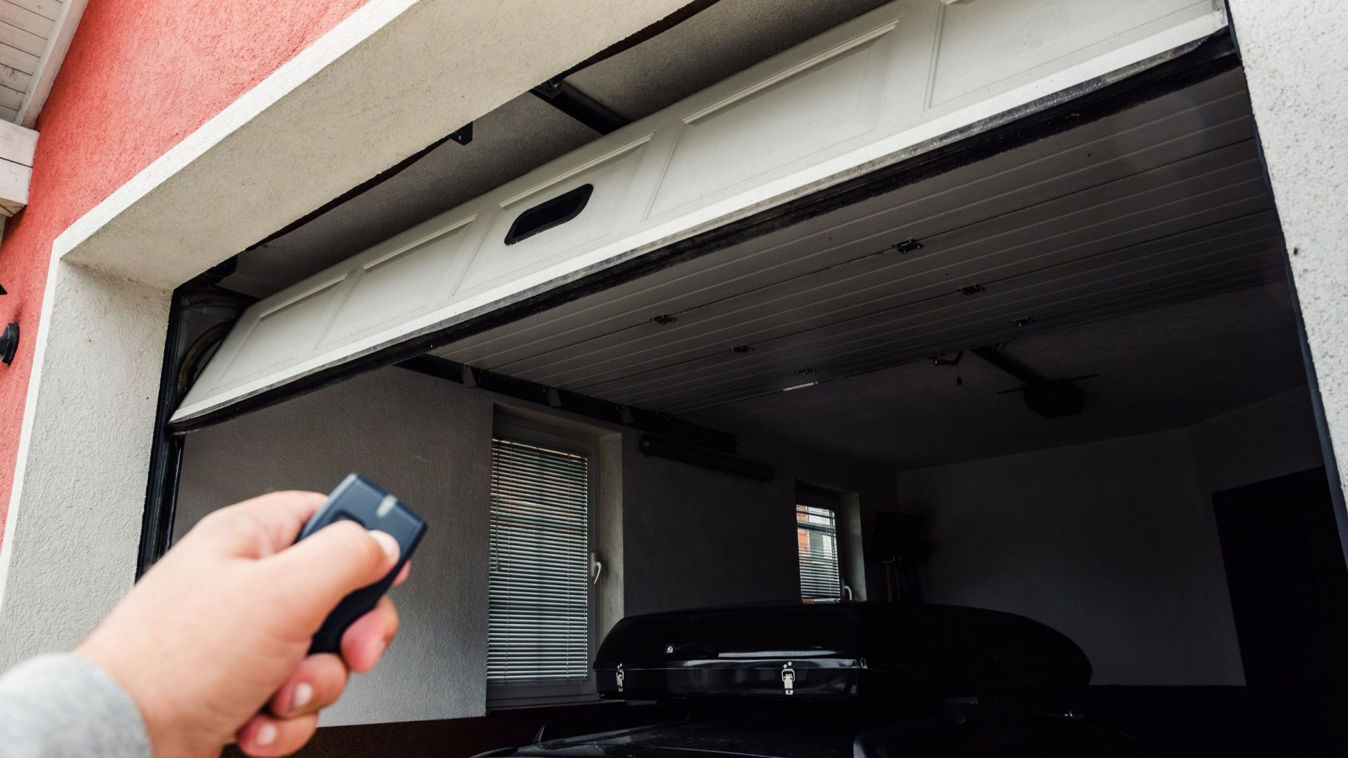 A hand holding a fob opening a garage door remotely.