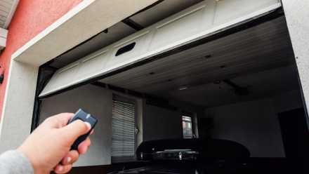 A hand holding a fob opening a garage door remotely.