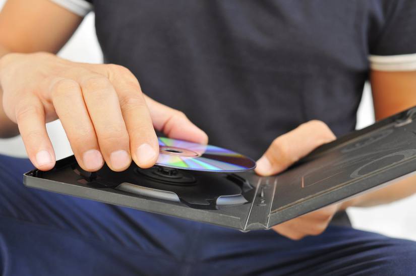 Closeup of a young man pulling a DVD or a CD out of its case.