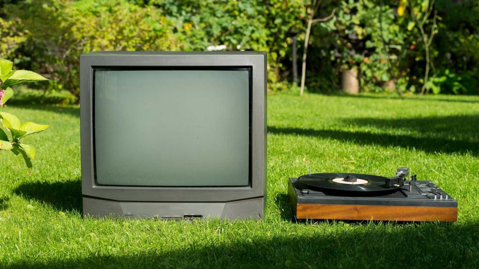 Um tocador de TV e discos vintage um ao lado do outro no gramado.