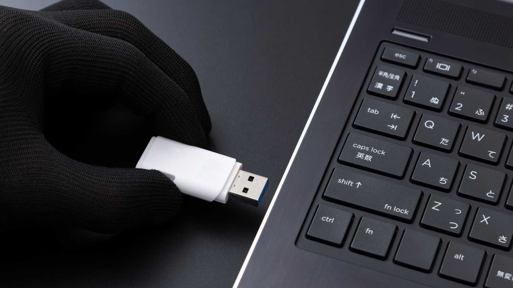 Uma mão enluvada insere uma unidade USB em um laptop.