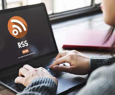 A woman sits in front of a laptop showing the RSS logo.