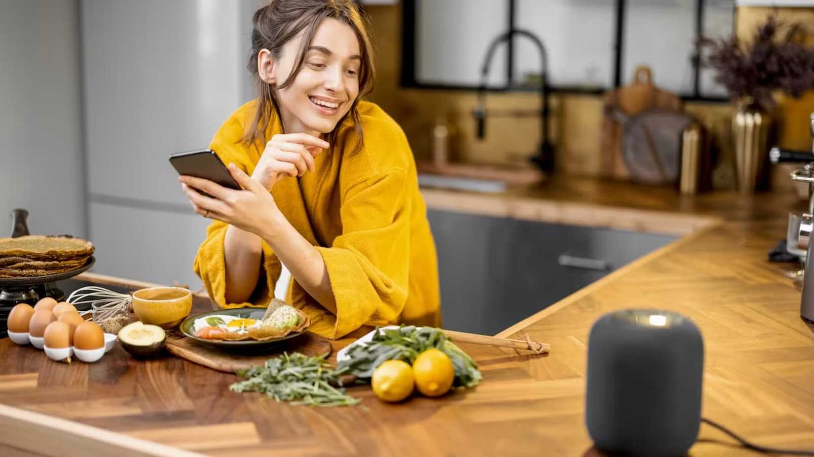 Woman in a kitchen using voice commands to control a smart speaker.