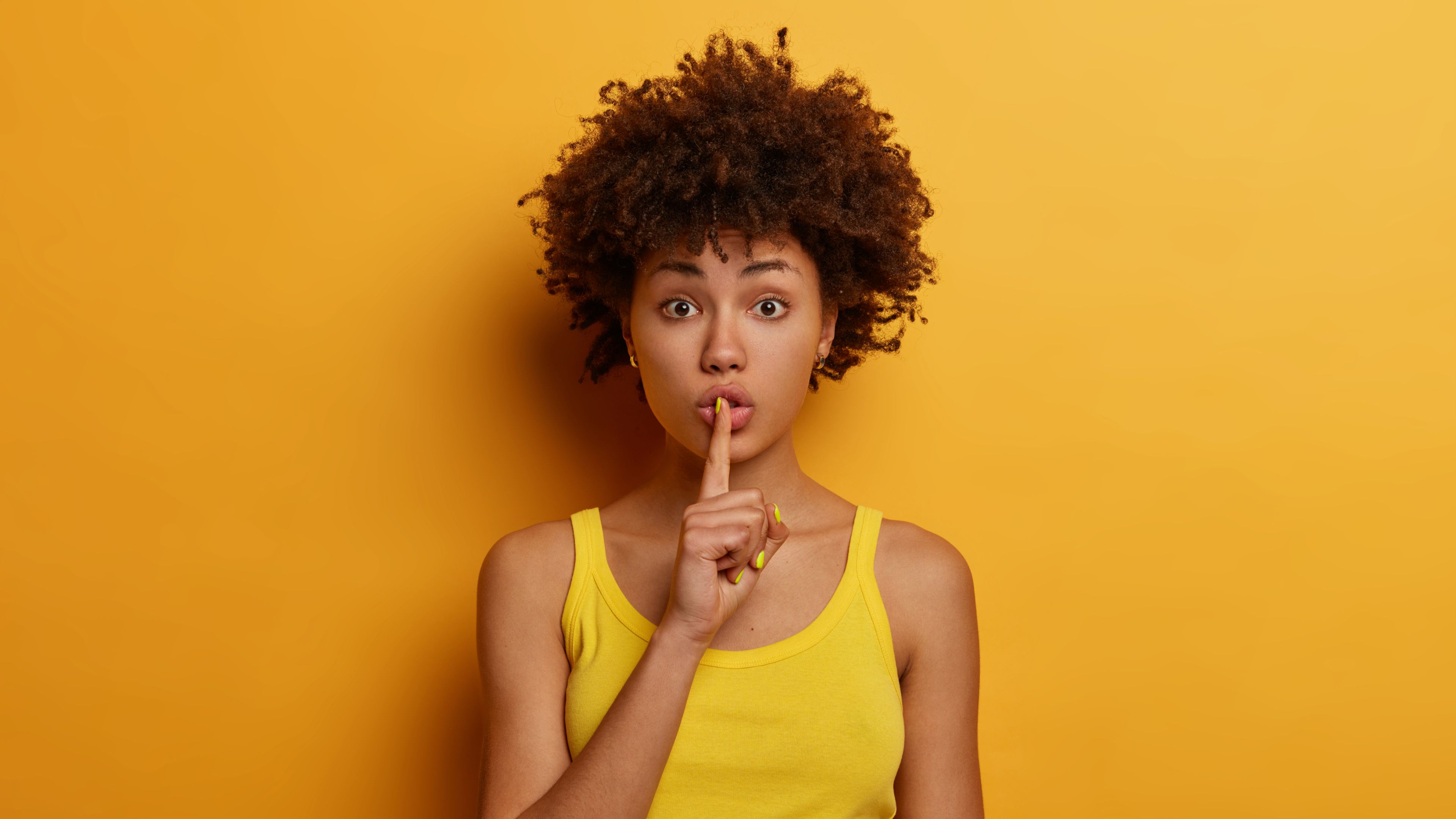 Young woman on a colorful background with a finger to her mouth in a shush motion.