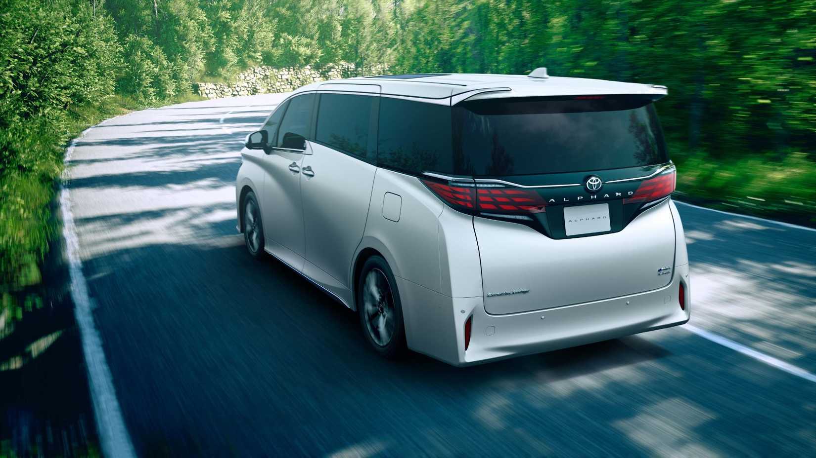 Dynamic rear 3/4 shot of a 2024 Toyota Alphard driving on a country road lined by trees.