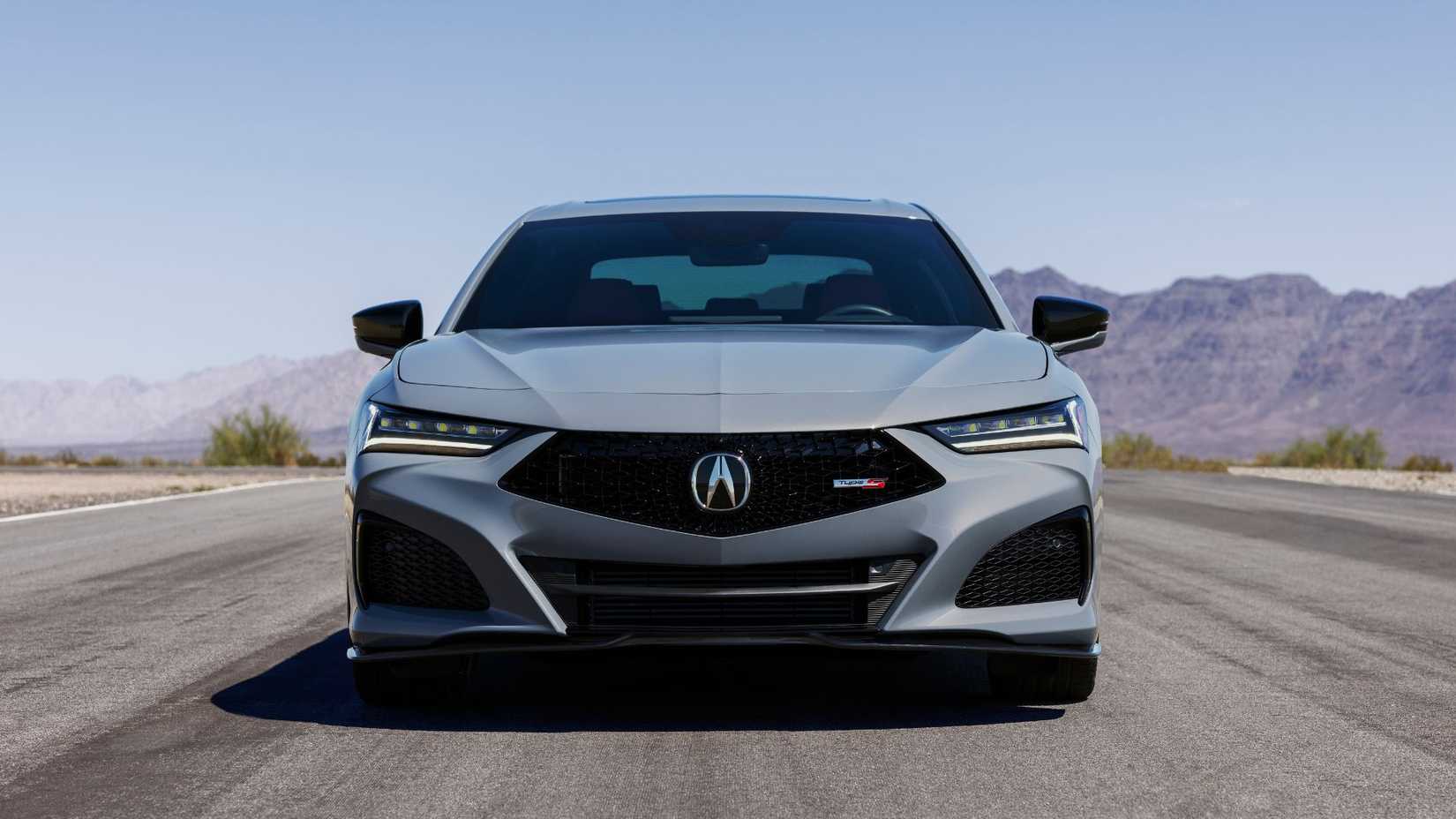 Dynamic front-end shot of a gray 2024 Acura TLX Type S driving on a road with mountains in the background.