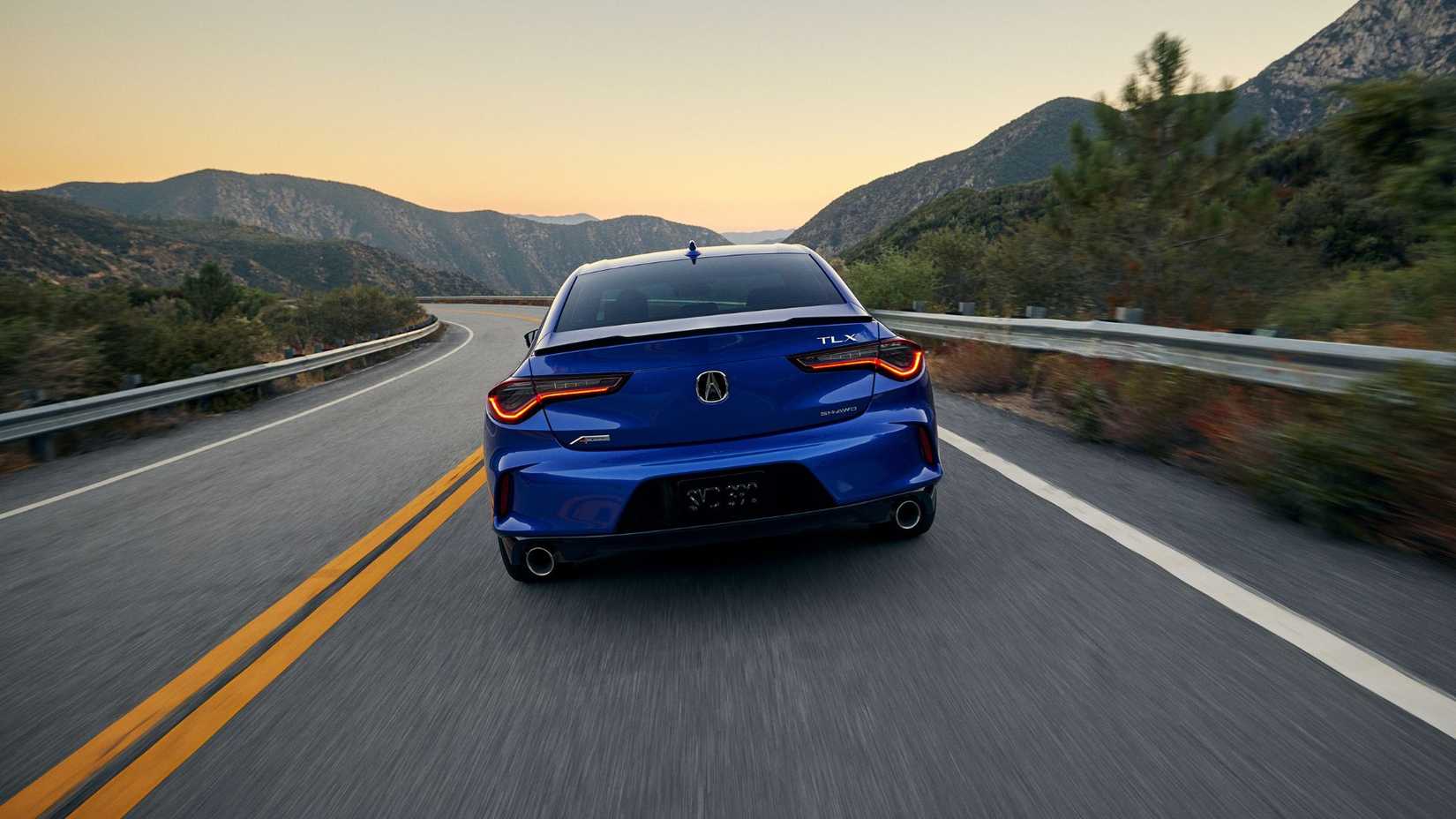 Dynamic rear-end shot of a blue 2024 Acura TLX A-Spec driving on a winding country road.