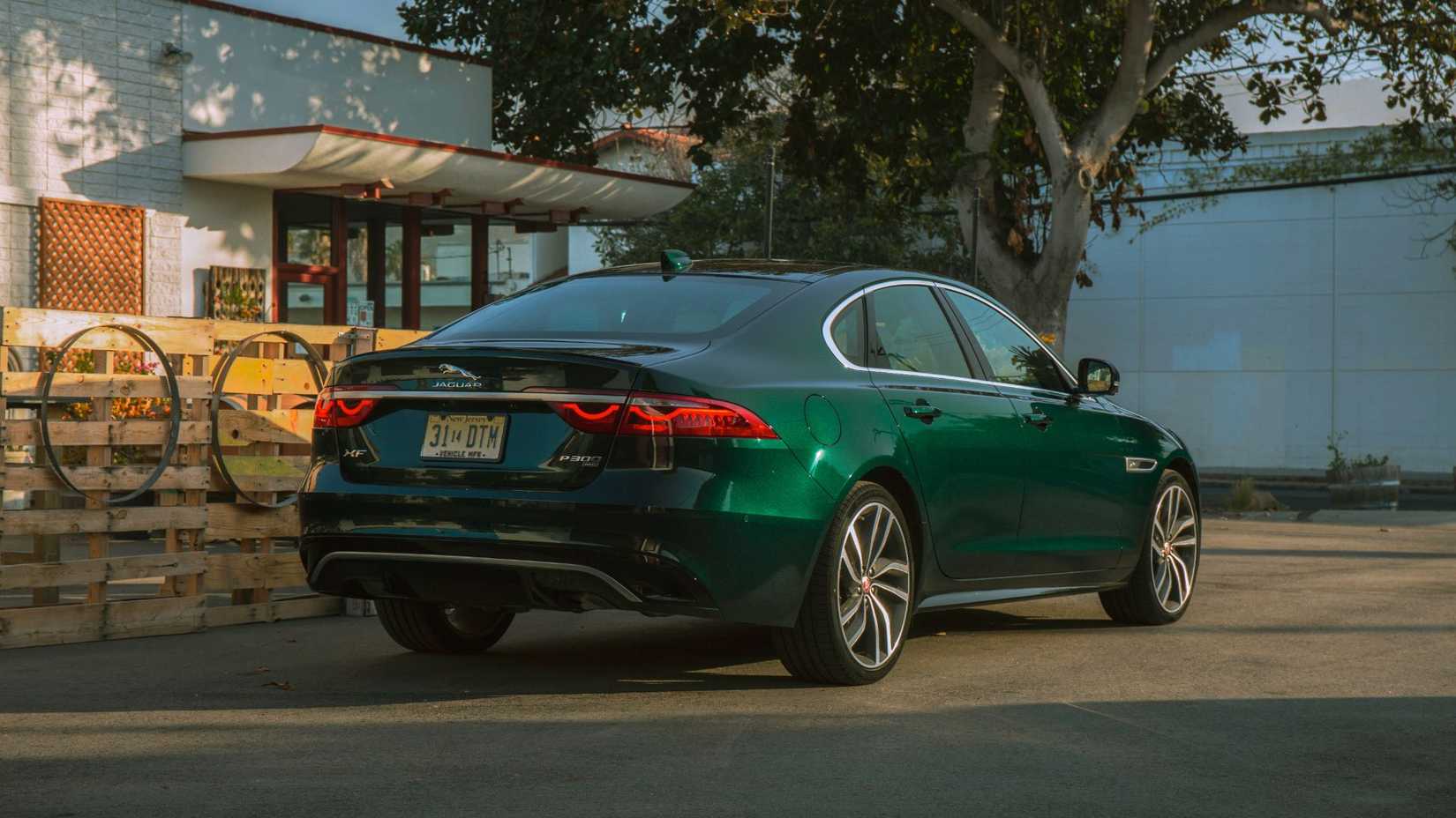 Traseiro estático 3/4 de um tiro de um green 2021 Jaguar XF P300 R-Dinamic Se estacionado ao lado de uma cerca de madeira.
