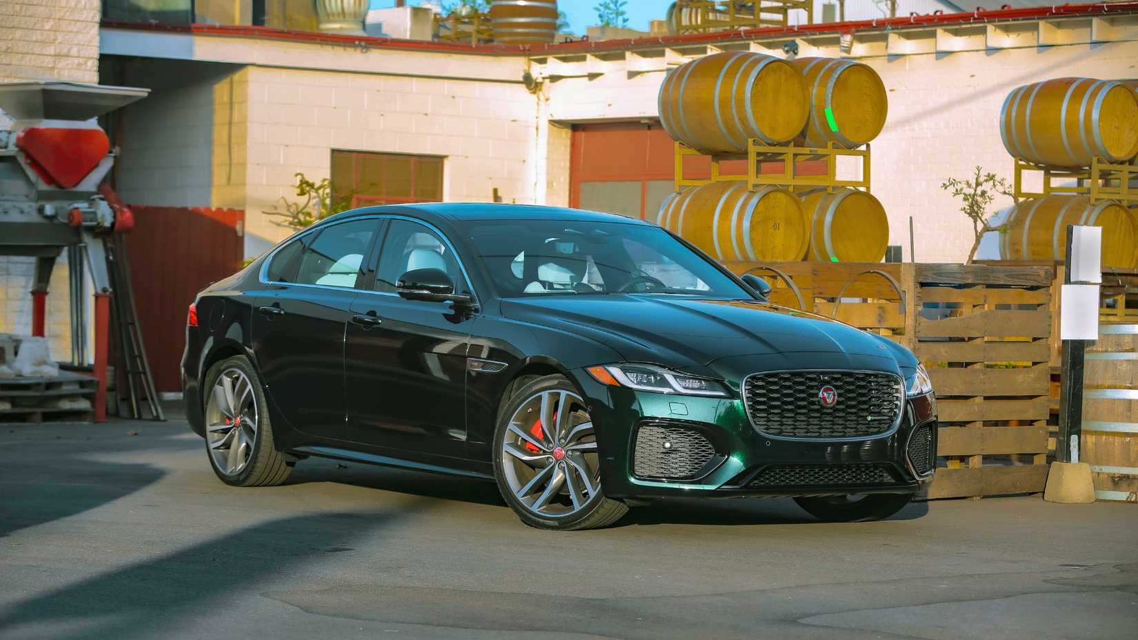 Static front 3/4 shot of a green 2021 Jaguar XF P300 R-DYNAMIC SE parked with barrels in the background.