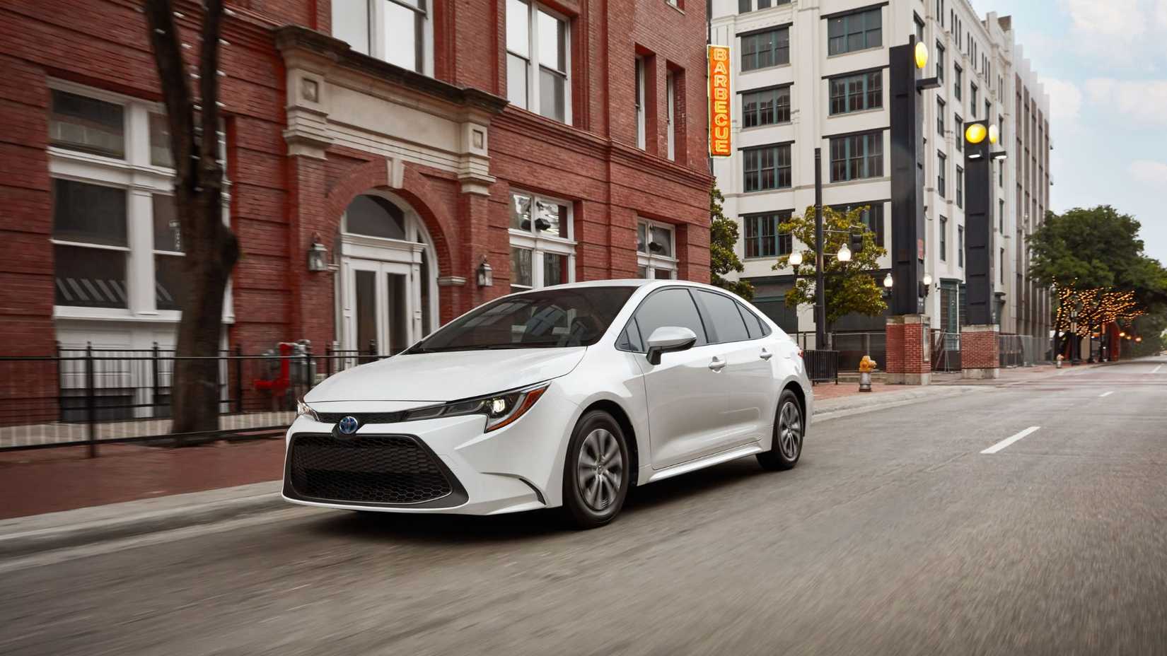 Dynamic front 3/4 shot of a white 2022 Toyota Corolla Hybrid driving in a city.