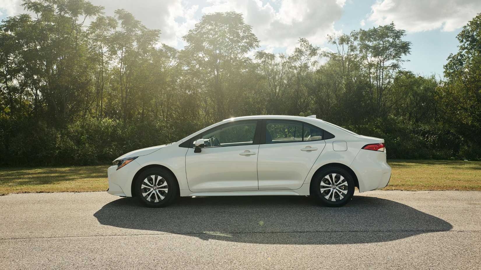 Static side profile shot of a white 2022 Toyota Corolla Hybrid parked with trees in the background.