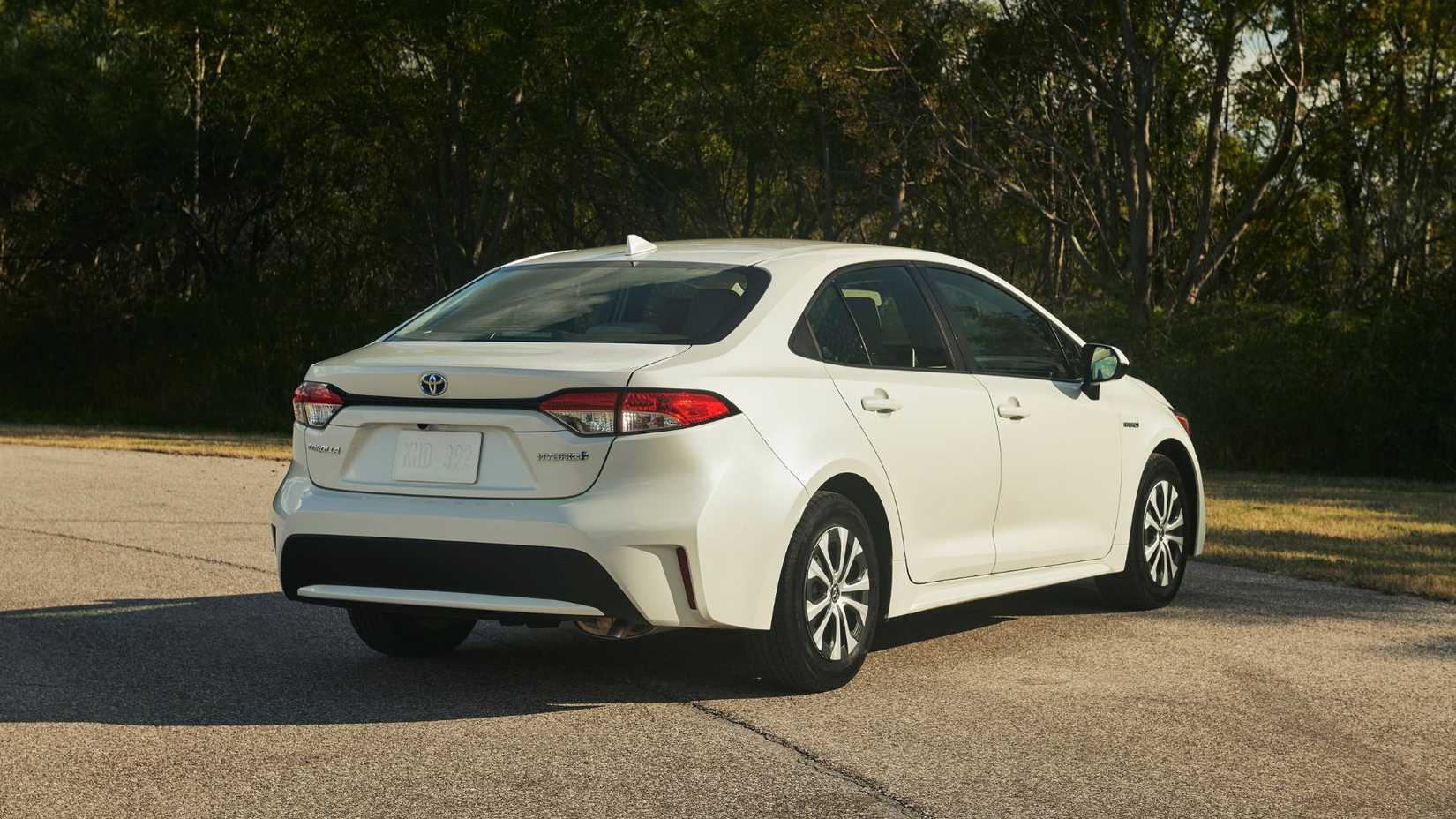 Static rear 3/4 shot of a white 2022 Toyota Corolla Hybrid parked with trees in the background.