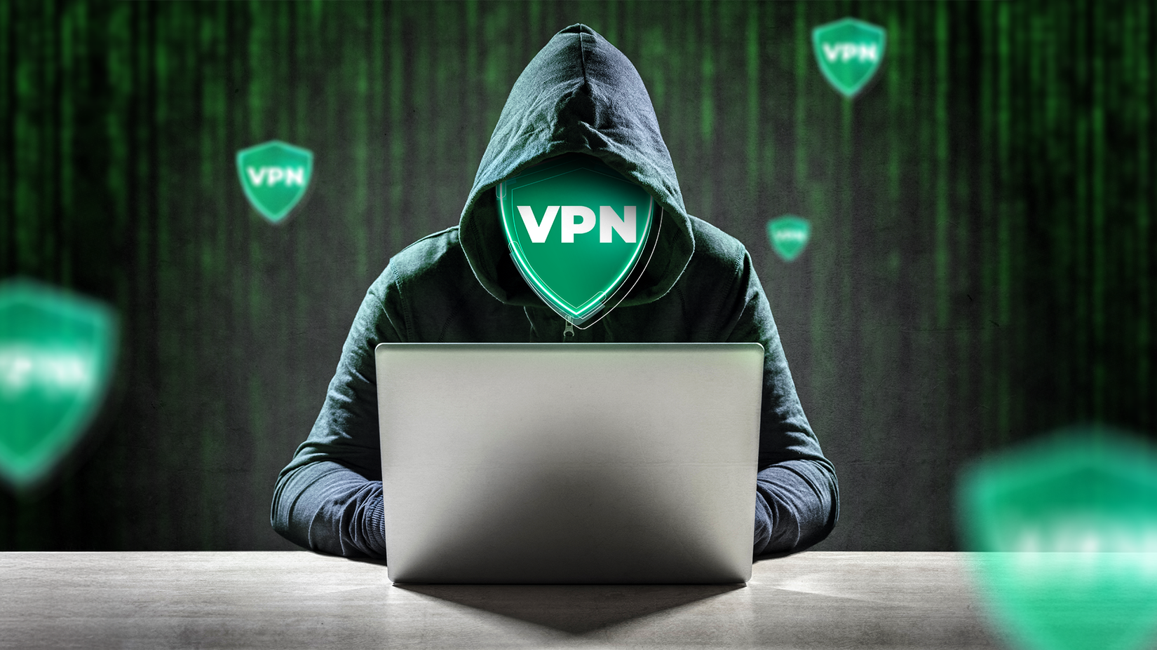 A hooded person using a laptop, with a glowing green VPN shield for a face and multiple VPN shields floating in the background.