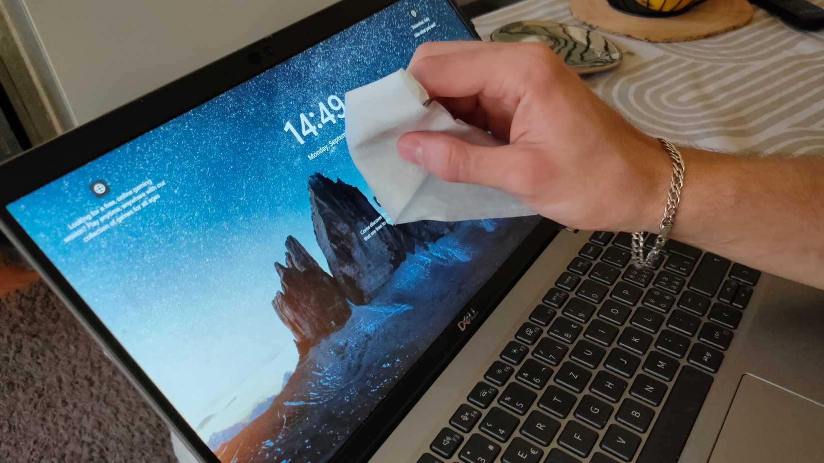 A hand wiping a laptop screen with a wet wipe.
