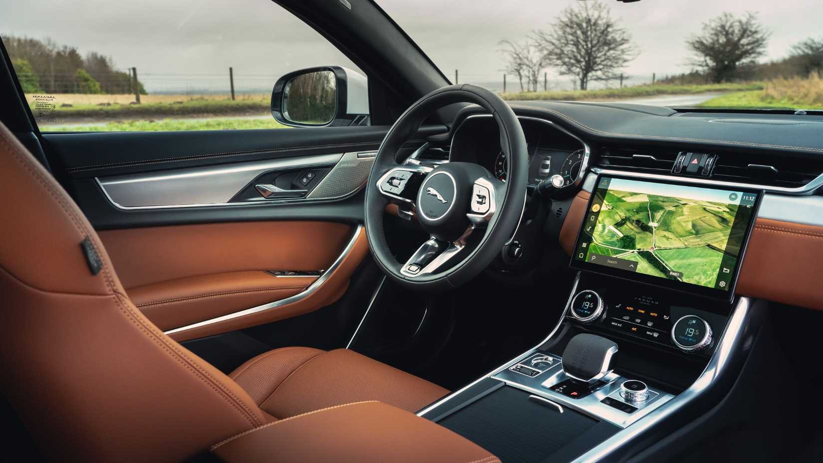 Filmado dentro da cabine de um Jaguar XF de 2021, mostrando o assento do motorista de couro marrom, o volante e a tela de infotainment.