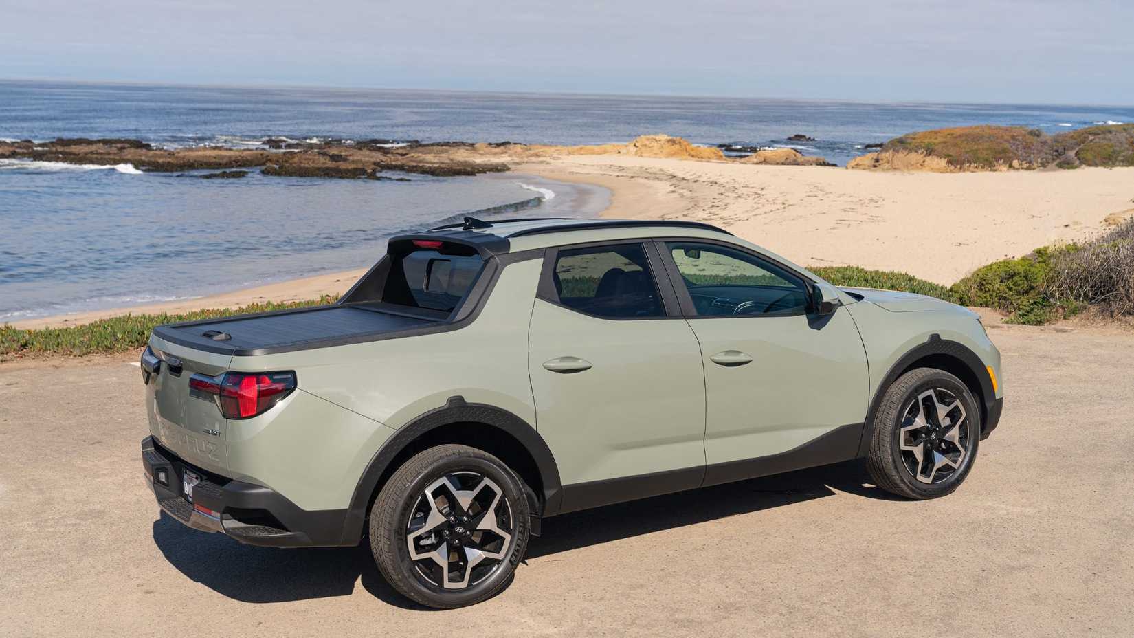 Static side profile shot of a green 2024 Hyundai Santa Cruz parked on gravel beside the ocean.