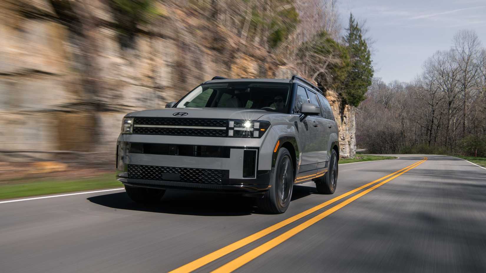 Dynamic front 3/4 shot of a 2026 Hyundai Santa Fe driving on a country road.