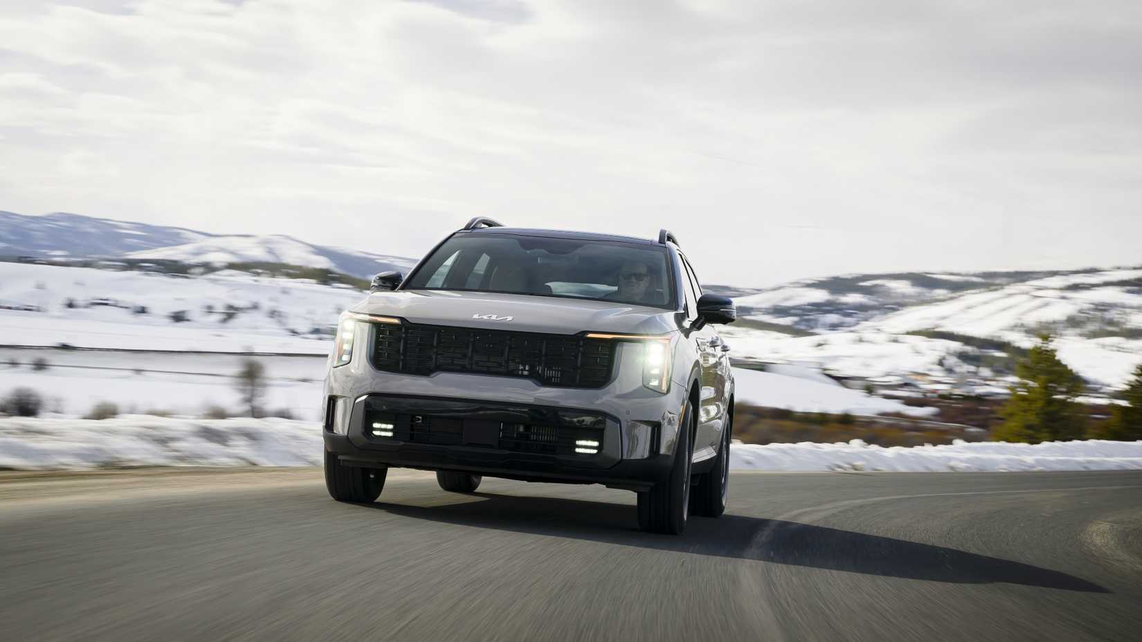 Динамичный снимок передней части автомобиля Kia Sorento 2026 года выпуска, едущего по заснеженной проселочной дороге.