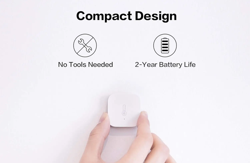 Uma foto do produto do Sensor de Temperatura e Umidade Aqara com uma mão segurando um deles preso à parede.