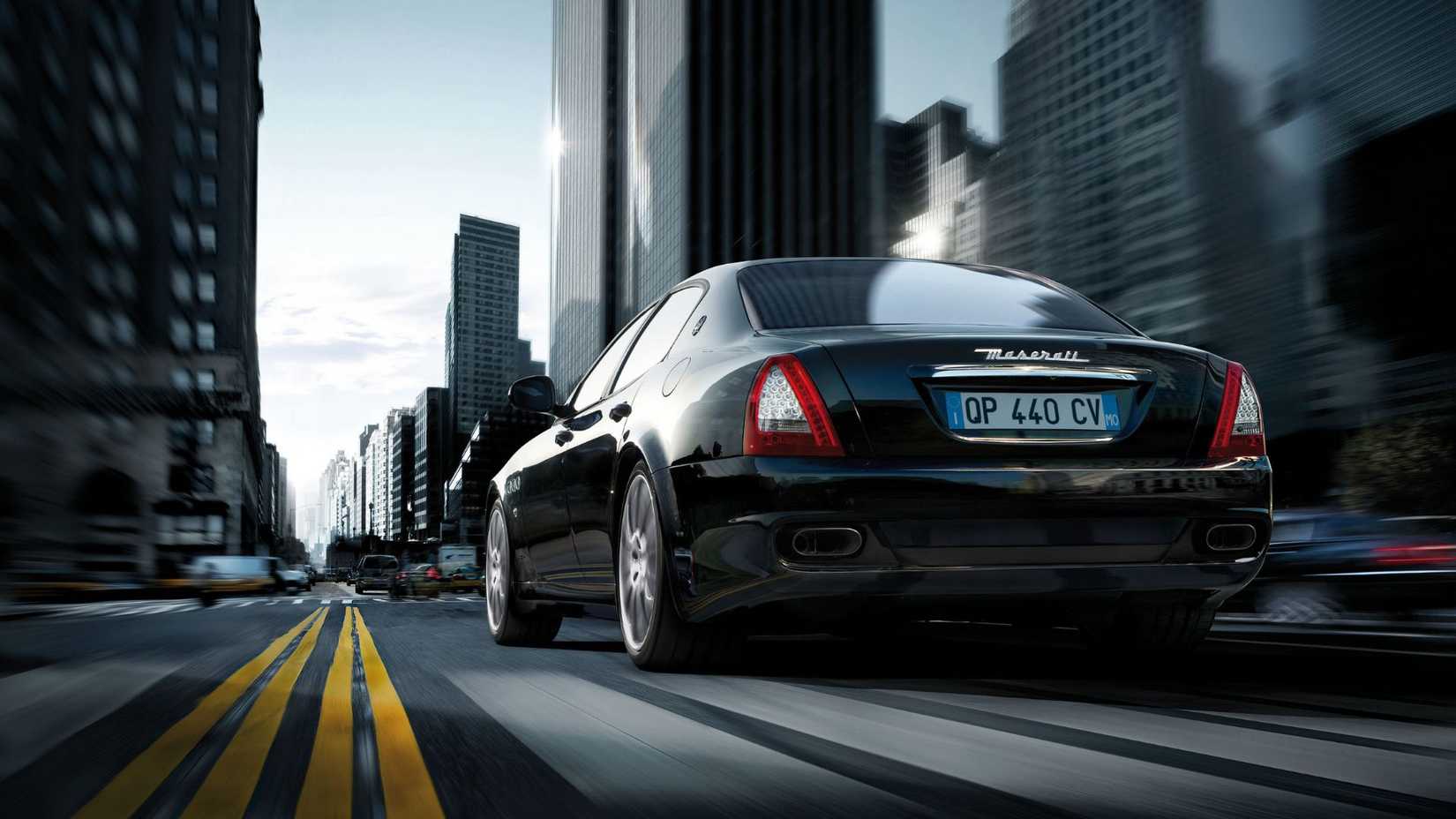 Foto traseira dinâmica 3/4 de um Maserati Quattroporte 2008 preto dirigindo em uma cidade.
