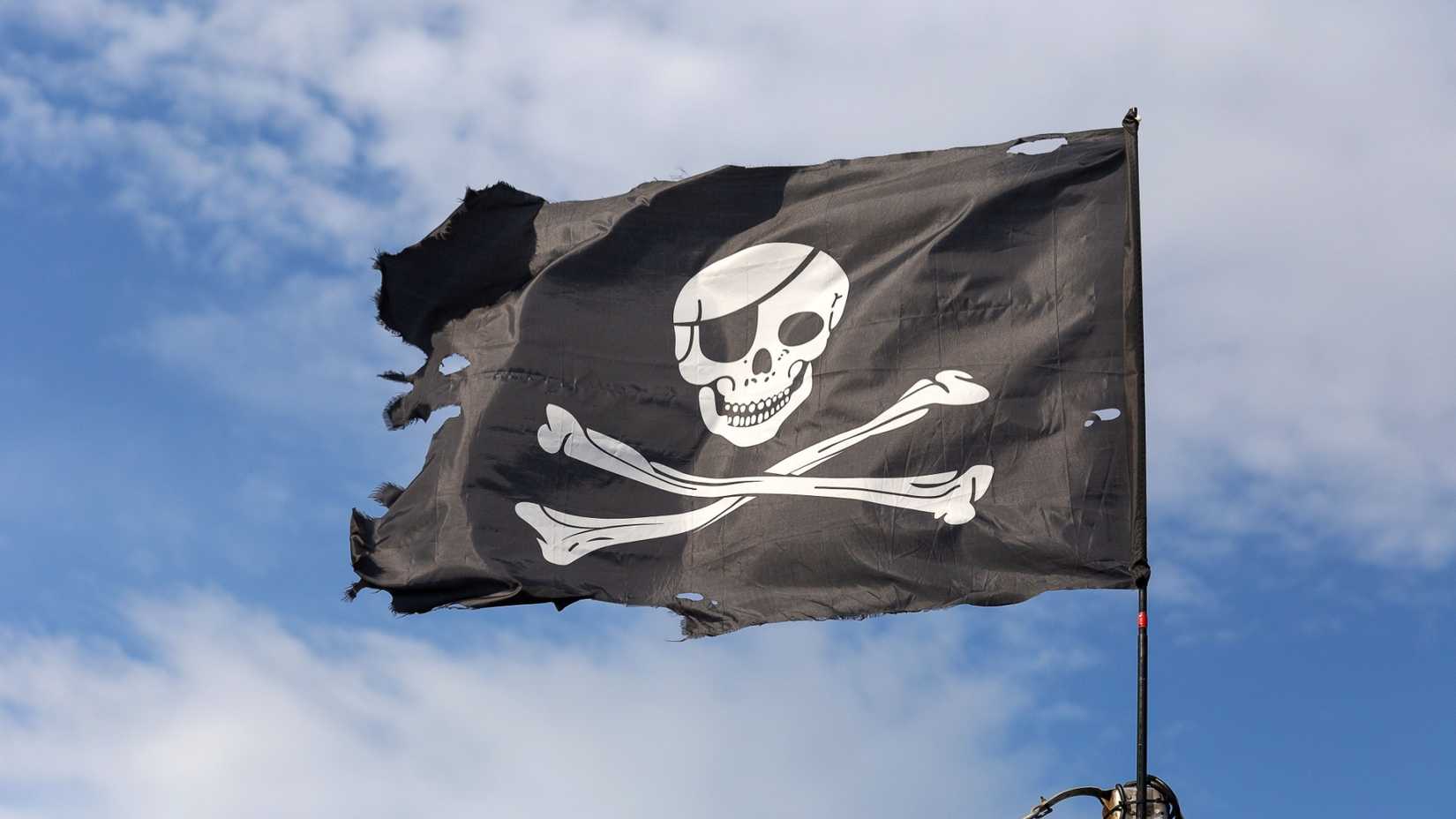 Jolly Roger pirate flag on blue sky background..