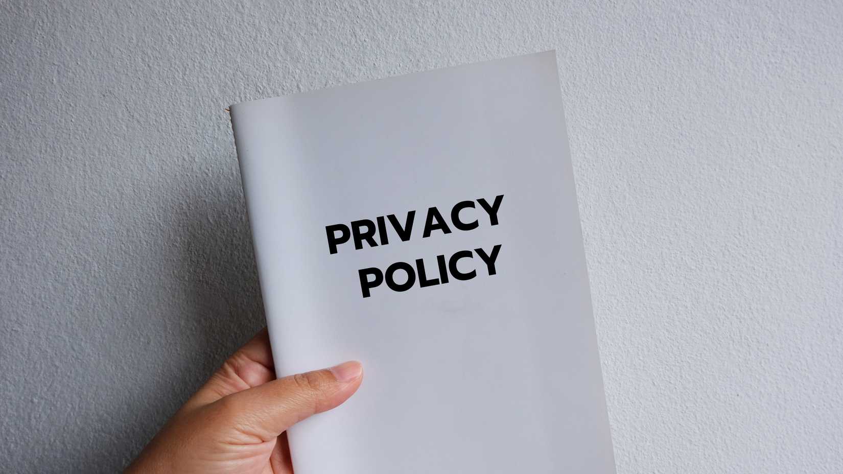 A hand holding a document with "Privacy Policy" written on the cover.