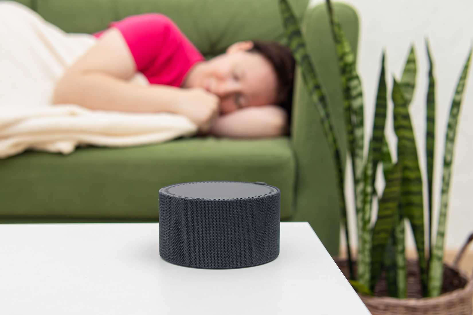 A woman sleeps on a couch next to a speaker making white noise.