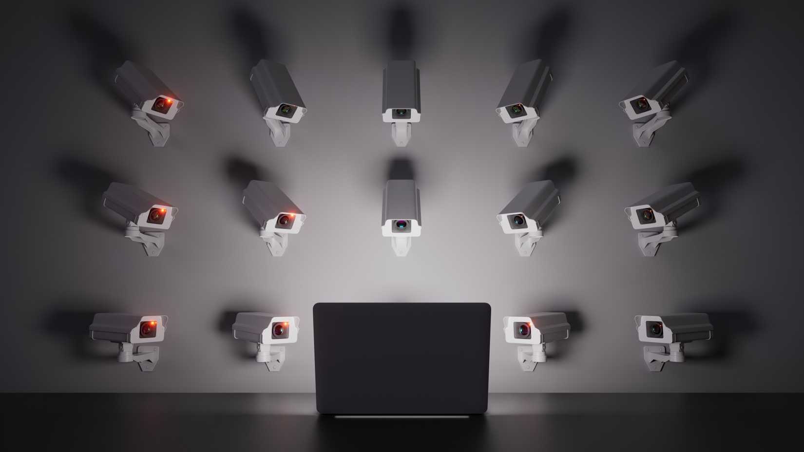 Wall-mounted cameras focus on a laptop screen, symbolizing surveillance and control.