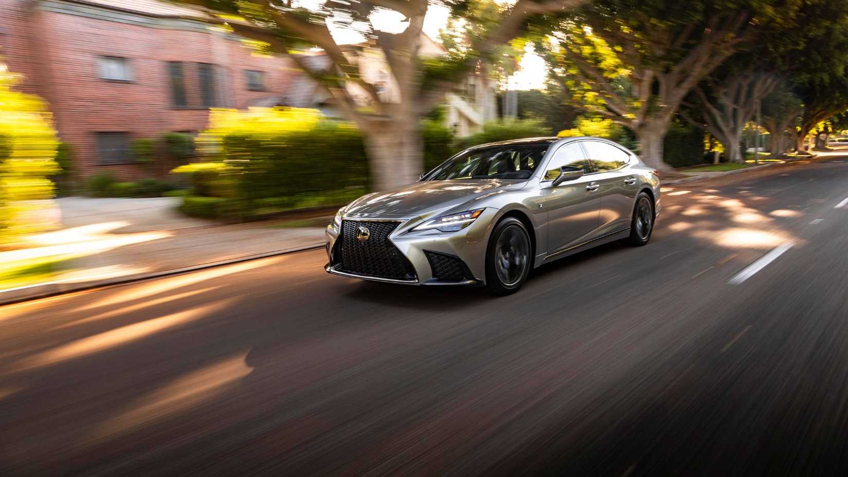 Dynamic front 3/4 shot of a silver 2025 Lexus LS 500 F-Sport driving in a city.