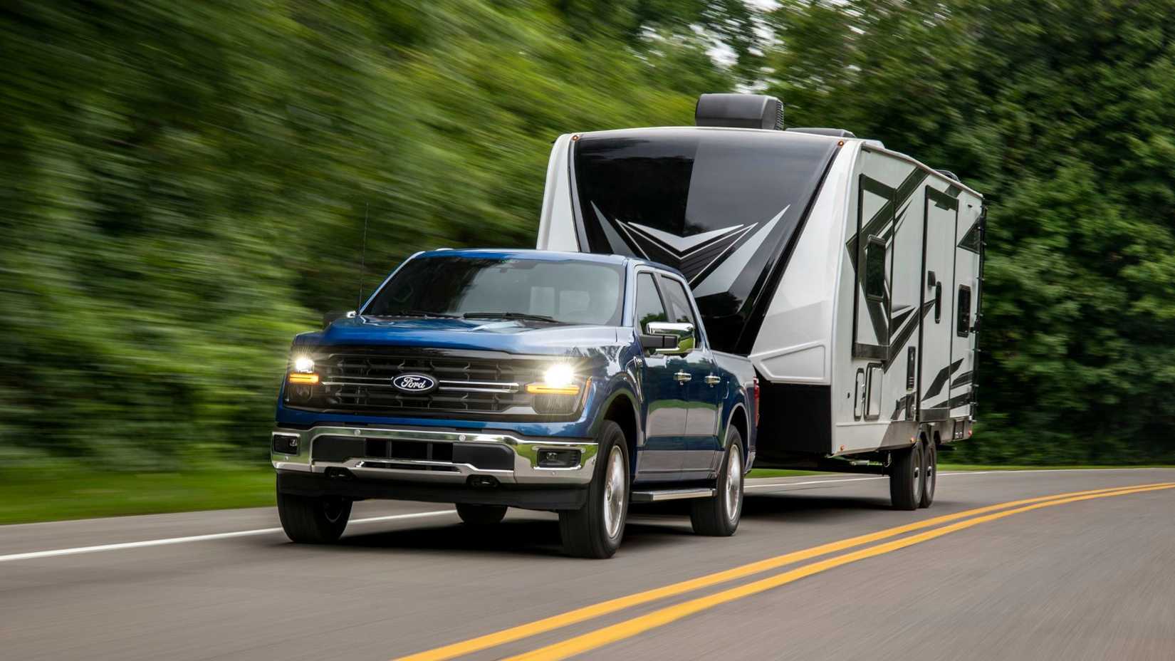 Dynamic front 3/4 shot of a blue 2024 Ford F-150 XLT towing a trailer.