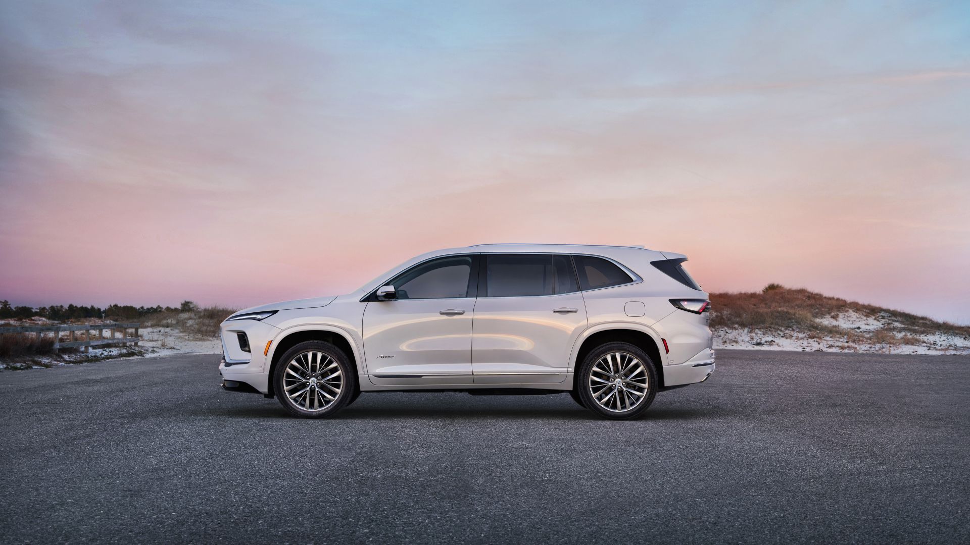 Static side profile shot of a white 2025 Buick Enclave Avenir parked on tarmac.