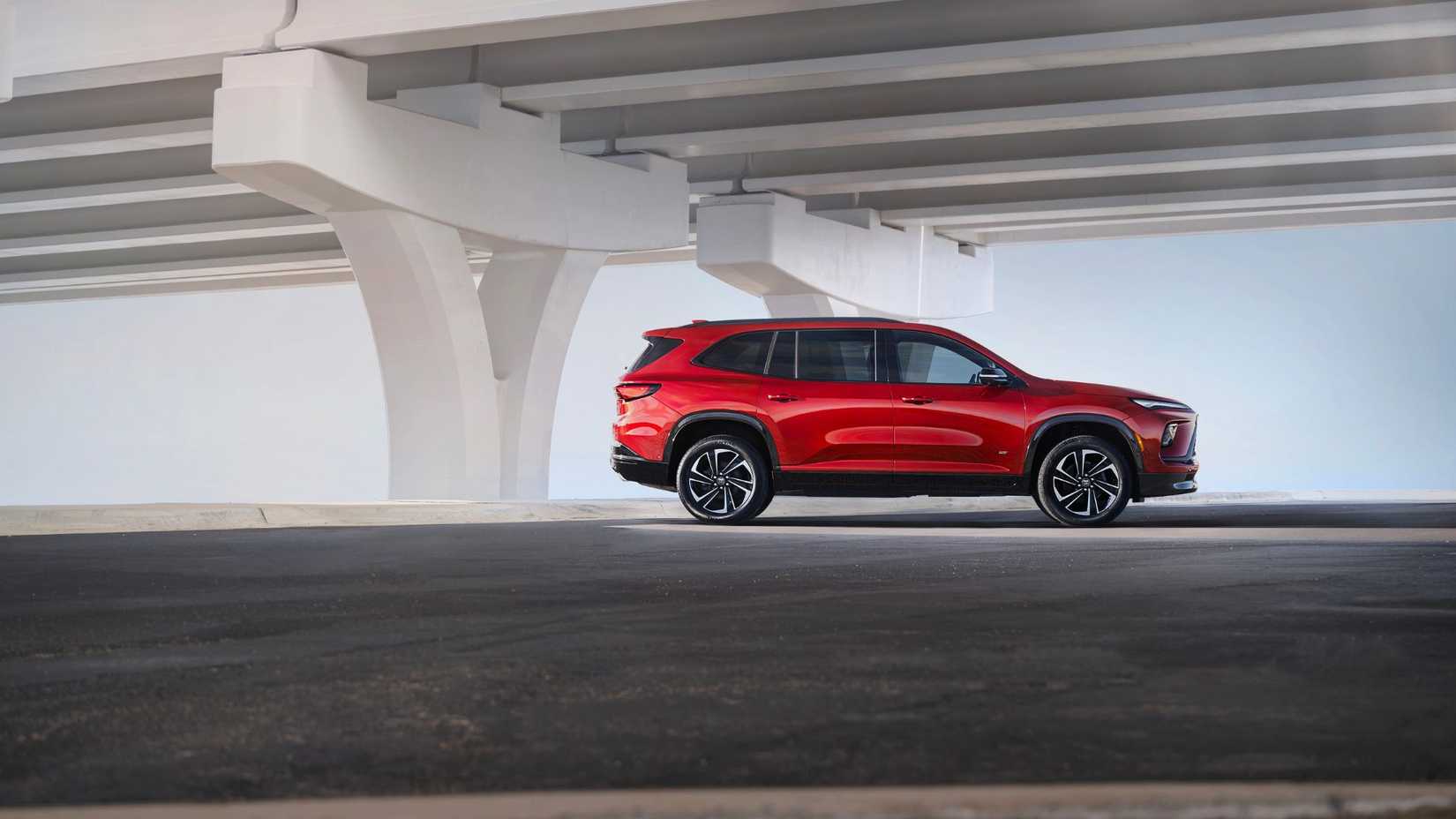 Static side profile shot of a red 2025 Buick Enclave Sport Touring parked underneath a bridge.