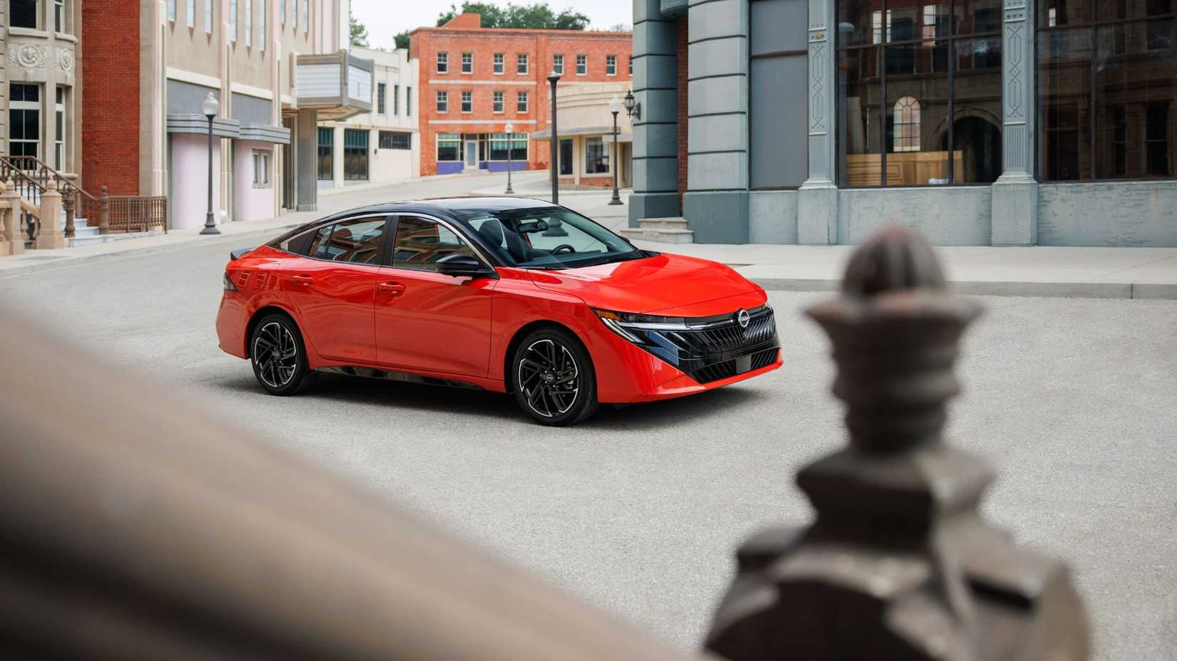 Static front 3/4 shot of a red 2026 Nissan Sentra parked in a city.