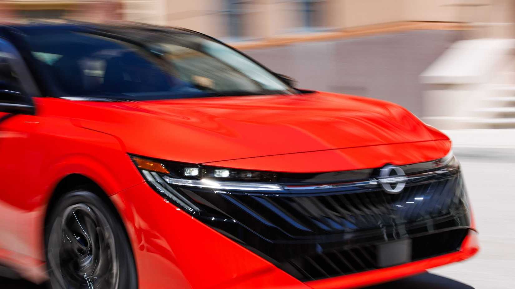 Close-up shot of the front end of a red 2026 Nissan Sentra driving in a city.