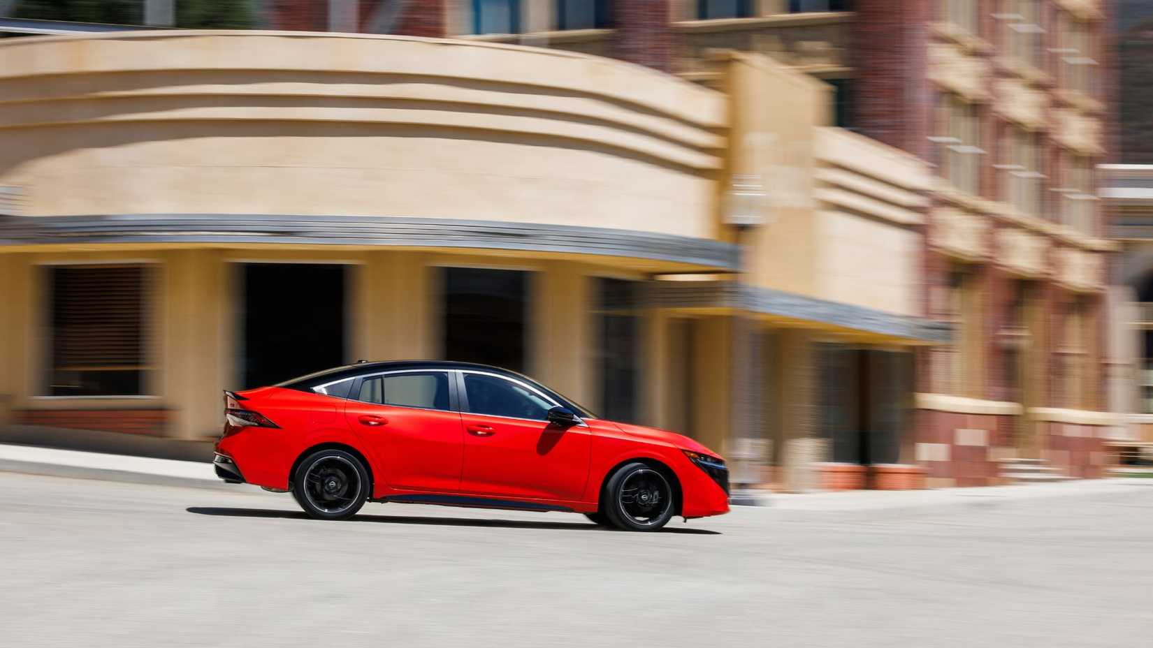 Dynamic side profile shot of a red 2026 Nissan Sentra driving in a city.